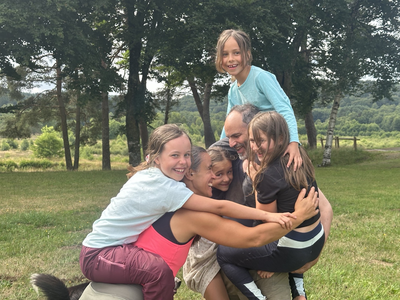 Câlin de groupe entre deux adultes et quatre fillettes, dans une prairie