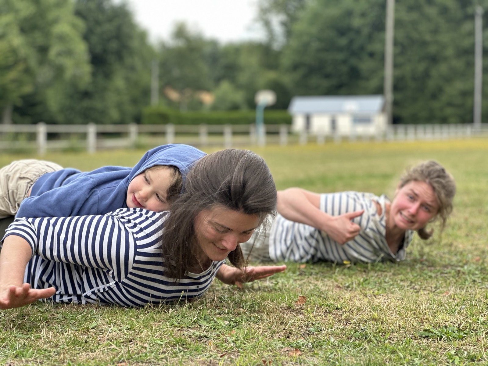 Trois personnes allongées bras tendus sur un terrain de sport, en riant